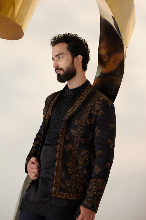 Black & Gold Short Jacket | Jatin Malik Presenting our striking all-black short jacket set, elevated with exquisite gold zari work and a distinguished shawl collar lapel detail. This ensemble exudes sophistication and modernity, making a bold statement with its sleek design and attention to detail. Paired with a short-length tone-on-tone kurta and tapered trousers, it offers a harmonious balance of style and versatility. Whether it's a formal occasion or a stylish gathering, this ensemble is sure to command attention and leave a lasting impression with its timeless elegance and impeccable craftsmanship. Included in purchase: Short Jacket, Kurta, Trousers Product Specification Color: Black Fabric: Linen Silk Occasion: Engagement, Wedding, Bridal, Reception Style: Short Jacket, Kurta, Trouse Jatin Malik, Wedding Kurta For Men, Blouse Yoke, Cute Celebrity Couples, Gold Shorts, Royal Look, Haldi Ceremony, Fashion Suits For Men, Tapered Trousers