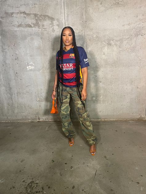 Parking garage outfitinspo, jersey outfit , black girl in braids with cargo pants and heels. Gold jewelry Women’s Soccer Jersey Outfit, Soccer Jersey Aesthetic Outfit, Cargo Pants And Jersey Outfit, Soccer Top Outfit Women, Jersey Outfit Ideas For Black Women, How To Style Soccer Jersey, Jersey Party Outfit Black Women, Soccer Jersey Outfit Women Aesthetic, Soccer Jersey Outfit Women Style