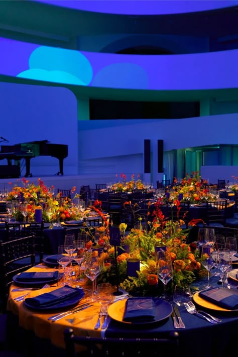 The table setting and scenography for the Guggenheim International Gala's dinner transformed the museum into a fantastical garden. Projections of flowers in an electric blue hue contrasted with the warmly lit tables for a colorful display of lights. From an aerial view, the Dior Maison table settings give the illusion that they are flowers themselves with illuminated centerpieces. © Reed Young Corporate Event Centerpieces, Dinner Table Set Up, Dinner Table Centerpieces, Dinner Party Table Settings, Colorful Centerpieces, Gala Themes, Corporate Dinner, Garden Centerpiece, Lighted Centerpieces