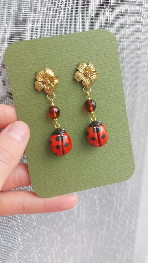 Handmade ladybug earrings, for someone who likes unusual jewelry. Ladybug is handmade from polymer clay and hand-painted. Cute golden flower together with brown glass bead creates vintage and earthy look. Length from the hook: 5.5 cm / 2.17 inches.  Earrings will arrive packed in cute decorative paper, so you will be able to gift them without the need for additional gift wrapping. Disinfect the hook before wearing. CARE INSTRUCTIONS:  Do not keep your earrings in direct sunlight as it may affect the metal color. Be gentle with your earrings; avoid playing with them or pulling on them. Do not bathe while wearing your earrings; keep them away from water. Keep earrings in a dry, shaded place. Keep each pair of earrings separate from each other because different types of metals can react, pote Polymer Clay Bug Earrings, Clay Earrings Air Dry, Flower Earrings Clay, Clay Bugs, Polymer Clay Snail, Clay Ladybug, Bug Earrings, Ladybug Earrings, Bug Jewelry