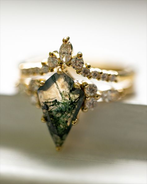 A "Sage" design engagement ring & matching tracer from Staghead Designs are shown. In the first photo, the ring is backlit with light shining through the center stone. In the second photo the ring is shown on a woman's finger. This 14K yellow gold engagement ring set features a kite cut moss agate center stone, round & marquise diamond accents, & a matching contoured diamond tracer with round & marquise diamonds. Jasper Engagement Ring, Moss Diamond Ring, Nature Engagement Rings, Raw Cut Engagement Ring, Miss Agate And Diamond Ring, Moss Agate Engagement Ring, Emerald Engagement Rings, Luxury Moss Agate Wedding Ring, Kite Shaped Engagement Ring Vintage