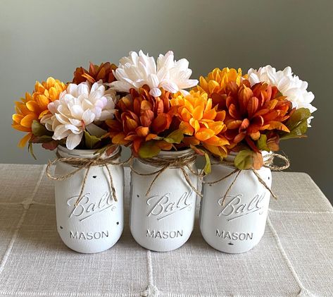 -Set of 3 hand-crafted chalk painted distressed Mason jar vases w/faux fall flowers included!  -Choose from colors in second photo. Mix & match Message me after purchase with color preferences.  -Add a bit of rustic charm to your home! Perfect for a gift idea, centerpiece, table top/seasonal decor, bridal or baby shower favors or decorations, wedding decor, housewarming gift, team/school colors, to brighten an office desk, bathroom or mantel.  -Jars are PINT size 16oz...5 inches high -Jars are w Fake Flower Centerpieces, Fall Harvest Party, Round Table Decor, Fall Mason Jars, Quart Size Mason Jars, Mason Jar Vases, Mums Flowers, Harvest Party, Centerpiece Table