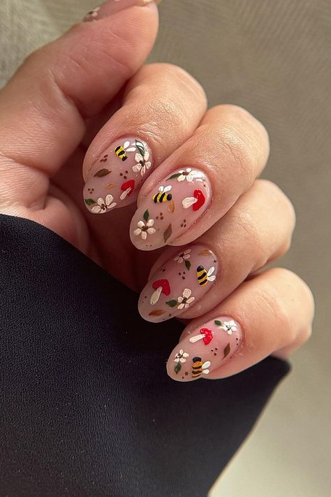 These almond-shaped nails are a whimsical ode to nature. A soft nude base is the perfect canvas for the intricate designs featuring buzzing bees, dainty white flowers, tiny red mushrooms, and subtle green leaves. The playful details bring an enchanting woodland vibe to your fall manicure. Adorable and charming!  // Photo Credit: Instagram @freshsetlancaster Mushroom Almond Nails, Woodland Nails Designs, Fall Themed Nails Simple, Nails With Mushrooms, Red Fall Nail Designs, Woodland Nails, Mushroom Nail Designs, Trendy Fall Nail Designs, Cottagecore Nails