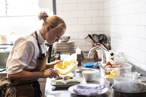 Female chef wearing brown apron standing at a kitchen counter, garnishing plate of asparagus. by Mint_Images. Female chef wearing brown apron standing at a kitchen counter, garnishing plate of asparagus. #Sponsored #brown, #apron, #standing, #Female Woman Washing Dishes, Dark Restaurant, Brown Apron, Chef Wear, Female Chef, Pose For The Camera, Restaurant Kitchen, Cooking Show, Washing Dishes