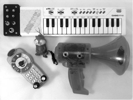 Figure 7-1: A selection of circuit-bent instruments and toys. Note the black box on the keyboard and the new bits on the other three: the knobs, switches, and bare metal contacts allow us to tinker with the toys’ pitch and tone on the fly, while the jacks allow us to amplify the output (and, in the case of the megaphone, pump our own signal into the input). Circuit Bending Instruments, Synthesizer Diy, Odyssey Of The Mind, Circuit Bending, Making Musical Instruments, Electronics Diy, Phone Jack, Instruments Music, Experimental Music