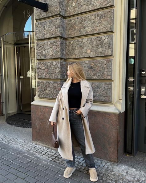 A blonde girl, standing in front of elegant building, she is wearing black jeans and black longsleeve, mustard seed ugg tazz and long beige coat Ugg Tazz Sand Outfit, Uggs Tazz Outfit, Beige Uggs Outfit, Sand Uggs Outfit, Tazz Ugg Outfit, Ugg Tazz Outfit Ideas, Outfit With Uggs, Europe Fits, Uggs Outfits