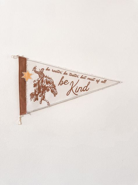 Add a dose of cowboy in your home with the "Rootin', Tootin', Be Kind" Pennant. A sheriff's star patch is added to give your flag a unique and dimensional look. Two layers of canvas fabric are sewn together for a durable, high quality feel. Display on wall easily with twine loops.  -Measures 10 x 18 inches Flag Pennant Banner, Cowboy Themed Nursery, Name Pennant, Word Art Wall, Rootin Tootin, Cowboy Decor, Pennant Flags, College Room, Custom Christmas Gifts