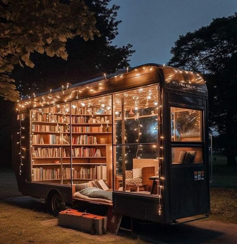 A pull along trailer that used to be enclosed, now has windows all over and inside is a library of books lining the walls. On the floor is a mat and setup to sleep, and in the corner a comfy chair. Little string lights line the top and sides of most of the windows while a large block of wood stands at the side as a stair. Mini Library Outdoor, Small Library Nook Ideas, Reading Shed, Book Van, Outdoor Library, Book Truck, Tiny Library, Forest Dark, Mobile Library