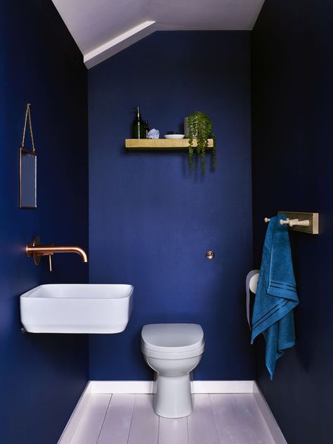 Dulux's Sapphire Salute is a deep and rich dark blue. Seen here in a small downstairs toilet/cloakroom, Sapphire Salute was voted the most popular paint colour for the bathroom, according to a study by luxury online bathroom retailer Drench. The metallic gold accents add a luxe feel while the wood shelving and towel rack calms the space. (Photo: Dulux) Sapphire Salute, Dark Blue Bathrooms, Small Downstairs Toilet, Most Popular Paint Colors, Small Toilet Room, Downstairs Loo, Downstairs Toilet, Toilet Room, Small Bathroom Makeover