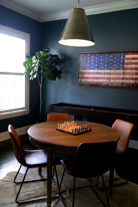 A moody masculine game room with game table, dark blue walls, shuffleboard table and leather and rawhide textures #gameroom #recroom #mancave Round Game Table And Chairs, Family Game Room Table, Game Table In Basement, Card Table Game Room, Game Tables In Basement, Elegant Game Room Ideas, Round Table Game Room, Game Table Room, Basement Table And Chairs