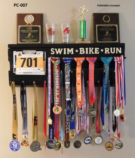 This is item #: PC-007 which measures 33" X 12 1/2". To display your medals it utilizes a glossy black rebar rod that is suspended under the almond colored words"Swim * Bike * Run." Additionally, two rows of brass hooks are on the bottom face board, while race bibs are held in place with a low-profile clamp. This solid award display unit is painted glossy black. Price: $125.00 Medal Board, Race Bib Display, Race Bib Holder, Race Medal Displays, Running Medal Display, Medal Displays, Workout Room Home, Race Medal, Running Medals