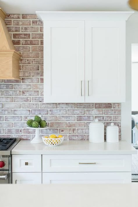 White shaker kitchen cabinets feature nickel knobs, white quartz countertops, and red brick backsplash tiles. White Kitchen With Brick, Whitewash Brick Backsplash, Red Brick Kitchen, Brick Kitchen Backsplash, Backsplash Kitchen White Cabinets, Brick Backsplash Kitchen, White Quartz Countertops, Rustic Backsplash, White Shaker Kitchen Cabinets