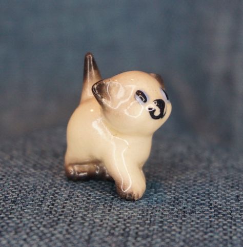 For sale is a miniature kitten figurine.  Below are more details about this item: *MATERIAL: ceramic *FINISH: glossy *COLOR: cream with brown accents; blue and black eyes  *MAKER: Hagen-Renaker; Designed by Helen Perrin Farnlund *TITLE/YEAR: "Siamese Kitten (nose up)" (1950-52)  *MARKS/LABELS: none *CONDITION: GOOD (no chips or repairs; some crazing)   *SIZE (approx.): 1 inch tall; 1 in. long *Coin Not Included *NOTE: Hagen-Renaker was a pottery company located in San Dimas, California from 1945 Chocolate Point Siamese, San Dimas California, Small Animal Figurine, Siamese Kitten, Fairy Garden Terrarium, Small Ceramic Animals Miniatures, Miniature Chocolate, Hagen Renaker, Calico Kittens Figurines