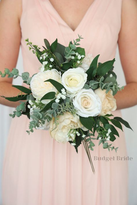 This rounded brides’ bouquet is elegant, understated, and perfect if you have chosen champagne or beige as one of the accent colors in your wedding. This beautiful bouquet does not fall short on class – there is plenty of lush greenery and accent foliage amidst the roses in off white and dazzling champagne and beige. Perfect for any bride who wants a sophisticated and classic look on her wedding day, this bouquet will stand out from the crowd. As usual, our bouquets are expertly crafted with car Simple Neutral Bouquet, Champagne And Greenery Wedding Theme, Diy Bridal Bouquet Fake Flowers, White Bridesmaid Bouquet, Champagne Bouquet, Elegant Wedding Bouquets, Simple Wedding Bouquets, Red Bouquet Wedding, Bridal Bouquet Flowers