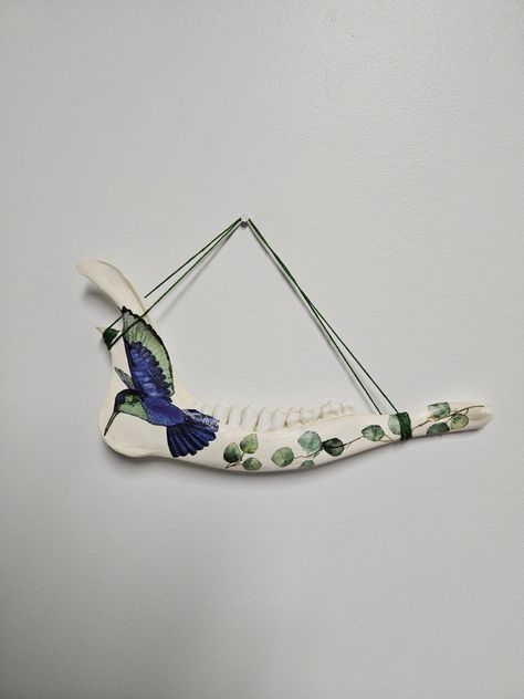 This is a hand made bone hanging wall decoration, using a real deer jaw bone. The blue & green hummingbird & floral details are added using decoupage.  The jaw bone is about 9" in length, the tallest part of the bone is 4.5" and the middle is about 1.5". Product care, it is not recommended to get the item wet, as this can cause the decoupage design to come off. Deer Jaw Bone Art, Jaw Bone Art, Green Hummingbird, Bone Art, Jaw Bone, Decoupage Art, Animal Bones, Hanging Wall, Halloween Shopping