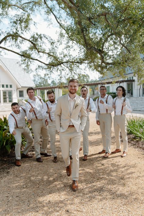 Groom walks toward the camera while groomsmen hype him up from behind Groom Attire Outdoor Wedding, Suspender Groomsmen Attire, Khaki Suit Groomsmen, Wedding Party Suspenders, Neutral Wedding Colors Groomsmen, Outdoor Wedding Party Outfit, Champagne Wedding Groomsmen, Tan Groom And Groomsmen Attire, Groom Suit Suspenders