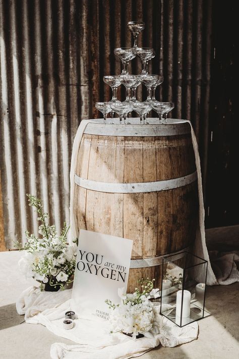 Champagne tower wedding decor on a wooden barrel with a frosted acrylic sign, drapery and white flowers Barrel Wedding Decor, Champagne Tower Wedding, Wine Barrel Decor, Wedding Cake Setting, Barrel Wedding, Fabric Installation, Cake Tables, Barrel Decor, Rustic Modern Wedding