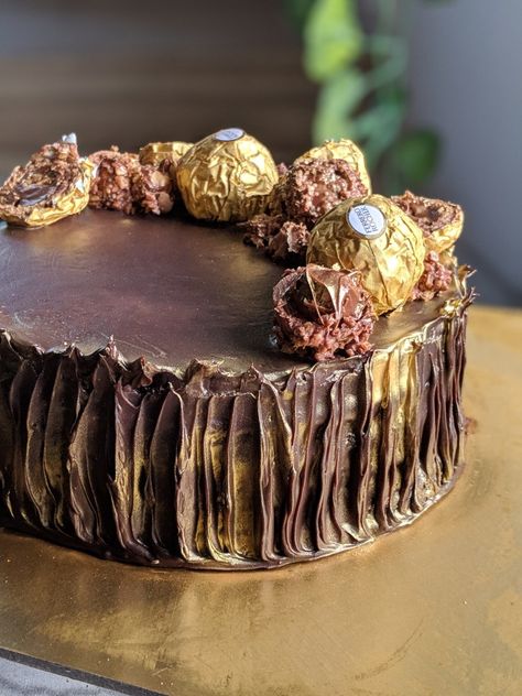 Ferrero Rocher cake| Isn't Chocolate like the bestestestessstest thing in the world? Made this impossible to resist Ferrero Rocher cake layered in Dark Chocolate Ganache and Nutella alternately, moistend with coffee Syrup  And loaded with ferrero Rocher Chocolate in between all the layers. Topped with Rochers and finished with golden dust. Texture: Melt in mouth dark chocolate cake with crunch in each layer! Flavours inside the cake: Chocolate ,coffee, hazelnut ! Selling at INR 2200/KG. Chocolate Cake With Ferrero Rocher, Ferrero Rocher Cake Design, Hazelnut Cake Design, Dark Chocolate Cake Design, Ferrero Cake, Simple Anniversary Cakes, Chocolate Birthday Cake Decoration, Classy Cake, Dust Texture