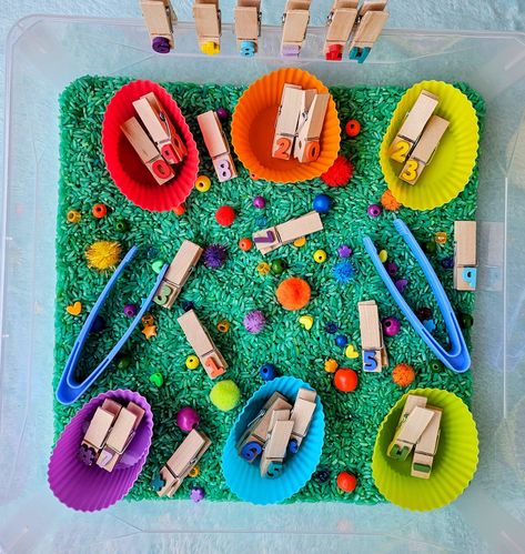 Our math and numbers themed Sensory Bin includes everything needed for hours of fun and learning!  Includes: bin with lid (11x8x2 inches), number and math signs ( +=-#) on woodned clips, tongs to work on fine motor skills, colored/dyed rice, an assortment of rainbow colored mix-ins to sort and silicon cups cups.  Always supervise children while playing with sensory bins. Bin color may vary slightly. Rice/sand/playdoh colors may vary slightly. Toys mary vary by color or shape (ex t-rex dino in pi Math Sensory Bin, Themed Sensory Bins, Christmas Gift Ideas For Teachers, Activities For Classroom, Dyed Rice, Numbers Activities, Math Signs, Sensory Play Toddlers, Gift Ideas For Teachers