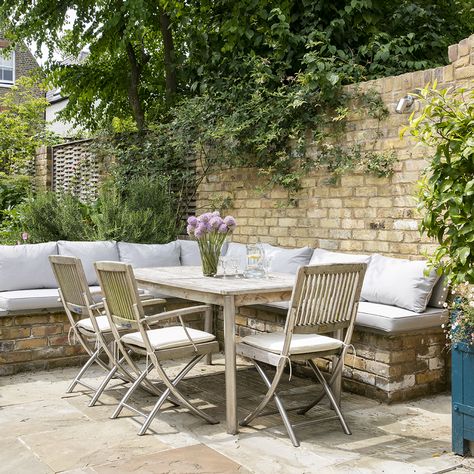 An L-shaped seating area has been built into this patio garden in a pale brick that mimics the colour of the brick wall. A pale wood and metal table and chair set complete the arrangement, with added cushions that provide comfort. A vase of flowers adds a pop of colour to the neutral scheme. Garden Seating Area, Country Garden Decor, Pale Wood, Garden Ideas Cheap, Country Cottage Style, Style Cottage, Dry Creek, Homestead Survival, Small Space Gardening