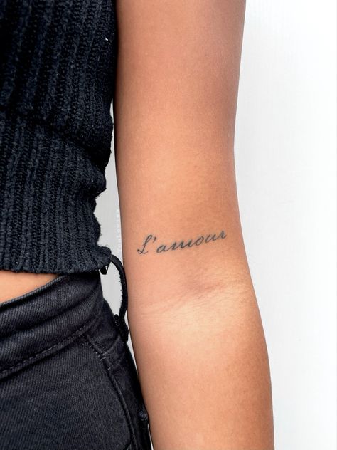 #tattoo #l’amour #love #smalltattoo #texttattoo #meaningfultattoos #tattoodesign Amour Tattoo Words, Tattoo Placement Names, Arm Text Tattoos For Women, Word Tattoo Placement For Women, Small Script Tattoo Placement, One Word Tattoo Placement, Small Word Tattoos Placement, Name Tattoo Arm, Text Tattoo Placement