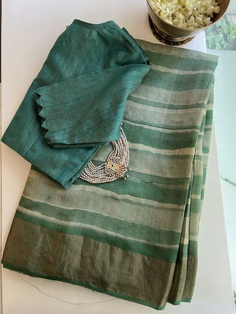 This dreamy saree is crafted from raw and lustrous pure handwoven tussar silk. Handprinted bands of green-hued stripes emulate the fluidity and translucence of watercolors and the deepsea. The addition of pure zari borders and a zari-striped pallu enhances the elegance of this sophisticated and ethereal drape. The saree comes with a floral printed green and beige blouse piece that is the perfect yin to the yang. Fancy Blouses Designs, Dreamy Saree, Elegant Saree Look, Striped Blouse Designs, New Dress Design Indian, Ikat Blouse Designs, Pure Tussar Silk Saree, Jute Silk Saree, Saree Styling