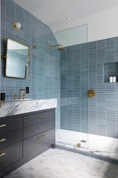 Bathroom features shower with stacked blue glass tiles, a blue tiled shower niche, aged brass shower kit, gray marble hexagon floor tiles and a glass partition next to a dark blue washstand topped in marble under a rectangular pivot mirror. Blue Shower Tile, Blue Glass Tile, Blue Bathroom Tile, Shower Fixtures, Blue Tile, Shower Niche, Blue Bathroom, Blue Tiles, Bathroom Renos