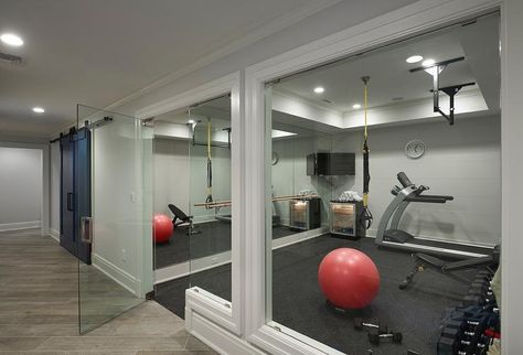 A glass door opens to a basement home gym filled with a mirrored accent wall lined with a corner flat panel tv over a freestanding glass door mini fridge. Home Gym Design Basement, Basement Home Gym, Basement Gym Ideas, Home Gym Basement, Contemporary Basement, Basement Home, Basement Gym, Basement Inspiration, Gym Room At Home