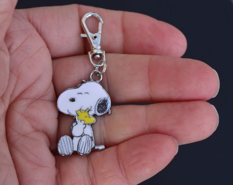 This is a great little zipper charm for the Peanuts or Snoopy/Woodstock lover to use on a backpack, gym bag, purse, planner, jacket, luggage, wallet, or cosmetic bag! Adorable Snoopy, holding a tiny Woodstock in his arms.  The enamel is bright white and yellow, all with silver accent. So adorable! Charm is one-sided.   Lobster clasp  9mm x 23mm. Clasp base swivels 360 degrees. *INTENDED FOR AGES 12 AND UP. SEE THIS LISTING FOR LARGER ENAMEL PEANUTS ZIPPER CHARMS. CHARLIE BROWN, SALLY, AND PEPPER Snoopy Accessories, Snoopy Merchandise, Snoopy Items, Snoopy Gifts, In His Arms, Peanuts Cartoon, Snoopy Woodstock, The Peanuts, Snoopy Love