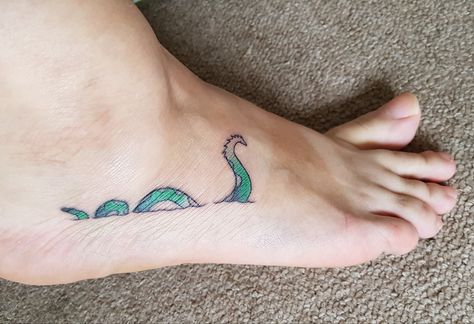 Loch Ness Tattoo. I like to think this wee Scottish monster is a little whimsical but badass. Lock Ness Monster Tattoo, Lockness Monster Tattoo, Loch Ness Monster Tattoo, Nessie Tattoo, Cryptid Tattoo, Scotland Tattoo, Scottish Thistle Tattoo, Thistle Tattoo, Monster Tattoo