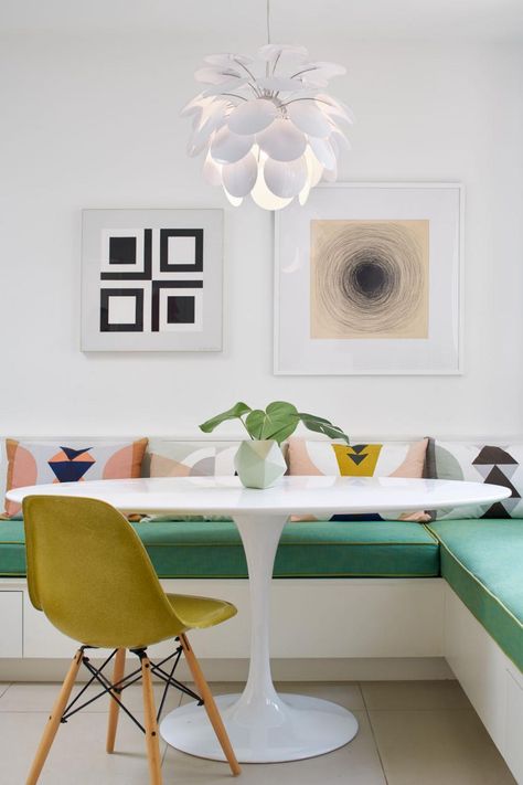 This clean-lined white home features bursts of color along with midcentury modern flair. Large windows allow ample natural light, which is supplemented by creative light fixtures including a Sputnik chandelier. Unusual features, such as a tall, carved fireplace surround in the living room, add visual interest to the home. Seating In Kitchen, Mid Century Dining Room, Banquette Seating In Kitchen, Kitchen Banquette, Kitchen Seating, Tulip Table, Banquette Seating, Mid Century Dining, Dining Nook