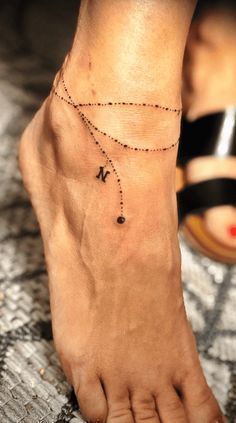 Tattoo Ideas Anklet, Name Charm Bracelet Tattoo, Ankle Bracelet Tattoo With Initials, Tattoo Ideas Female Leg Ankle, Ankle Bracelets With Names, Woman Ankle Tattoo Ideas, Ankle Charm Tattoo, Tattoo Anklet Bracelet, Ankle Bracket Tatoos