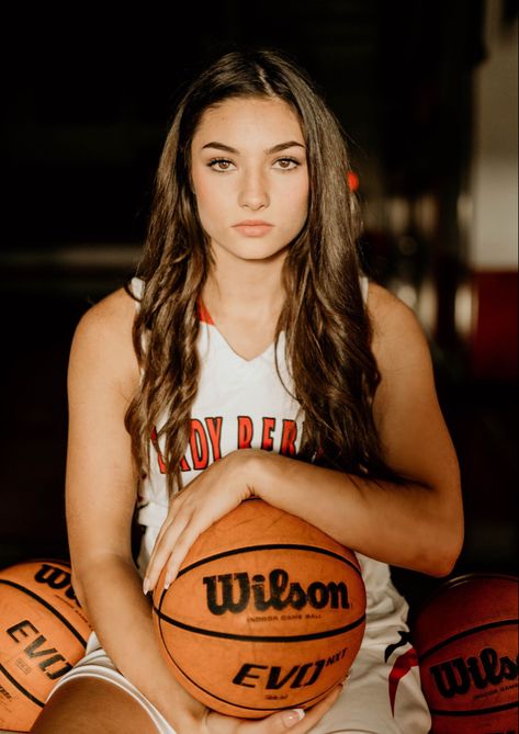 Girl sitting on basketball rack holding a basketball with a serious face. Basketball Court Photography, Senior Basketball Photography, Cool Basketball Pictures, Basketball Photoshoot, Basketball Team Pictures, Hoop Backdrop, Basketball Pictures Poses, Basketball Banners, Sports Photoshoot