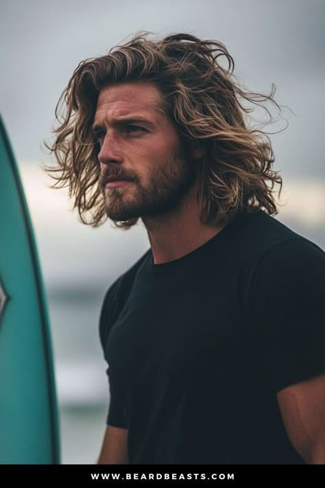 Man with textured, wavy hair and a rugged beard, standing by the beach with a surfboard, embodying the effortless, windswept look of men's hairstyles for long hair. This carefree surfer style perfectly captures a laid-back, adventurous vibe, ideal for beach lovers and outdoor enthusiasts. Long Hair Sides Shaved Men, Surf Haircut Men, Mens Beach Hair, Men Wavy Long Hair, Long Men’s Hair, Men’s Long Hairstyle, Viking Hairstyles Men Long Hair, Mens Long Hairstyles Wavy Thick Hair, Surfer Haircut Men