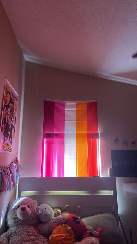 Lesbian flag over a window above a bed with stuffed animals and posters on the wall. Lesbian Flag Decor, Pride Flag In Bedroom, Room With Lesbian Flag, Lesbian Flag Bedroom, Lesbian Flag Room Decor, Lesbian Flag Room, Lesbian Room Ideas, Lesbian Room Decor, Lgbtq Bedroom