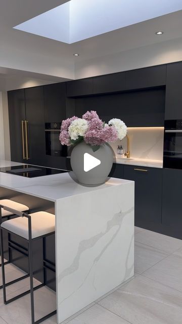 Lauren Barker on Instagram: "Monochrome! With a splash of pink and a hint of gold! We love our black kitchen design! It’s so easy to change up with different faux flowers too!  Barstools are from @by_crea use the code LAURENB10 for discount on all their modern furniture! . . . Large white Cleo vase is from @deargracehomeinteriors use the code BARKERSDEARGRACE for 15% off their website! . . . Floor tiles are the Sahara Blanco from @thetilecompanyltd  . . . Long gold handles are from @busterandpunch  . . . Faux flowers from @primark.home  . . . Monochrome kitchen design renovation 🖤 #kitchen #kitchendesign #openplanliving #kitchendecor #kitcheninspiration #kitchengoals #kitchenremodel #kitchenisland #quartz" Monochrome Kitchen, Ad Kitchen, Black Kitchen Design, Primark Home, 5 Days Left, Kitchen Clean, Classy Decor, Black Kitchen, Gold Handles