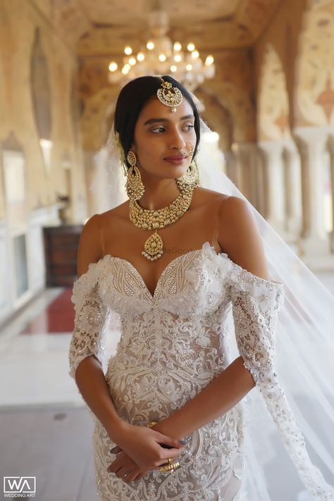 Such a unique way of pairing Indian traditional bridal jewellery on an off shoulder white gown| WedMeGood| #wedmegood #indianweddings #bridaljewellery #whitegown #traditionaljewellery #indianjewellery #gowns White Wedding Dress With Indian Jewelry, White Indian Bridal Dress, Indian Gold Bridal Jewellery, White Bridal Jewellery, White Wedding Dress With Gold Jewelry, Indian Inspired White Wedding Dress, Indowestern Wedding Dress, Indian And White Wedding, Sari Inspired Wedding Dress