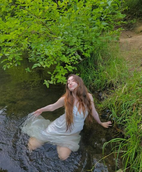 A girl in a while dress lays in the river, her dress wet surrounding her. The bank of the river is covered in grass and shrubbery. Water Nyphms, River Nymph Aesthetic, Water Nymph Photoshoot, White Dress In Water, Water Nymph Aesthetic, Tinker Bell Aesthetic, Bell Aesthetic, River Nymph, River Shoot