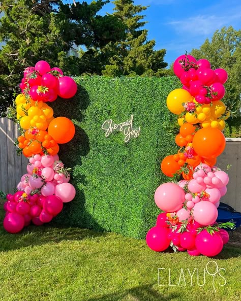 Bridal shower grass backdrop with colorful pink, orange and yellow balloons. Summer display Tiki Backdrop Ideas, Bright Colorful Centerpieces, Bright Pink Party Decorations, Balloon Garland Bright Colors, Pink Orange Yellow Balloons, Hawaiian Theme Balloon Garland, Hot Pink And Orange Balloons, Pink Orange Yellow Balloon Garland, Pink Yellow Orange Balloon Arch