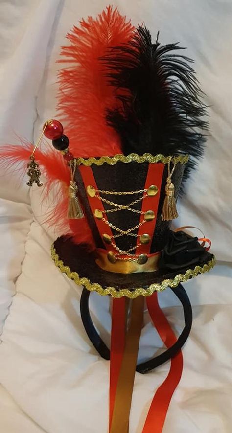 Circus Ringmaster mini black glitter top hat with satin headband. 1 x hatpin adorning pearls beads & a brass jester charm sits on side. Red & black ostrich feathers sit at back & a red chick feather & gold rooster feather sit on side. A black rose sits on other side & golden buttons are down front Circus Top Hat, Black Glitter Top, Circus Ringmaster, Jester Clown, Ringmaster Costume, Ring Master, Circus Dress, Circus Outfits, Lion Tamer