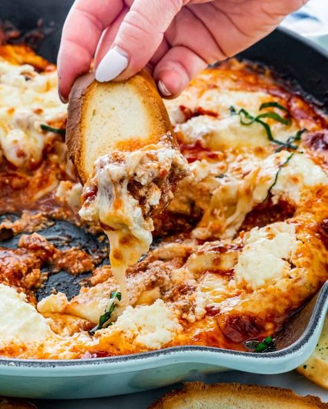 a hand dipping a piece of toasted bread into the lasagna dip Lasagna Dip Recipe, Lasagna Dip, Fresh Corn Salsa, Best Ground Beef Recipes, Best Dip Recipes, Baked Dips, Frozen Lasagna, New Year's Eve Appetizers, Appetizers Table