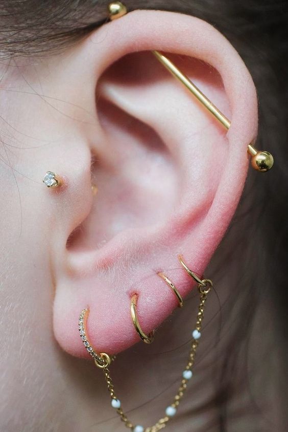 the ear is adorned with gold and white beads, which are attached to two different types of piercings