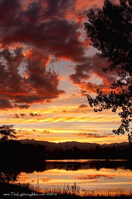 the sun is setting over a lake with mountains in the distance and trees around it