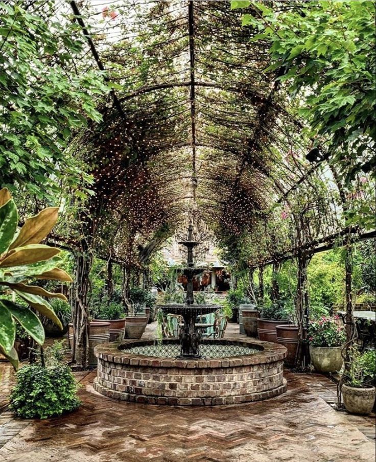 an outdoor fountain surrounded by trees and potted plants