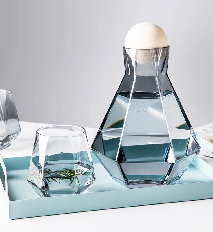 a glass vase with an egg in it sitting on a tray next to two glasses