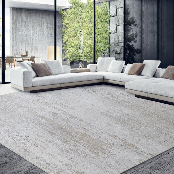 a living room with a large white sectional couch in front of a glass wall and floor to ceiling windows