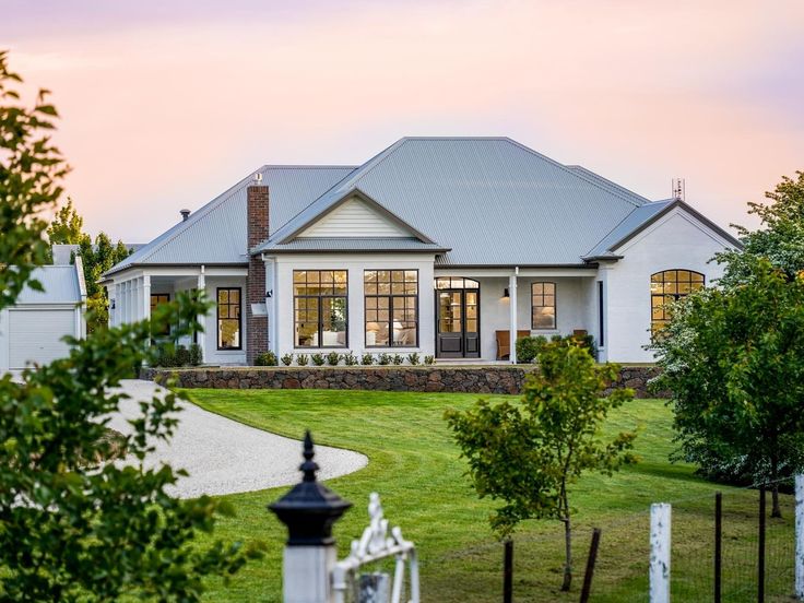 a large house sitting in the middle of a lush green field next to a white fence