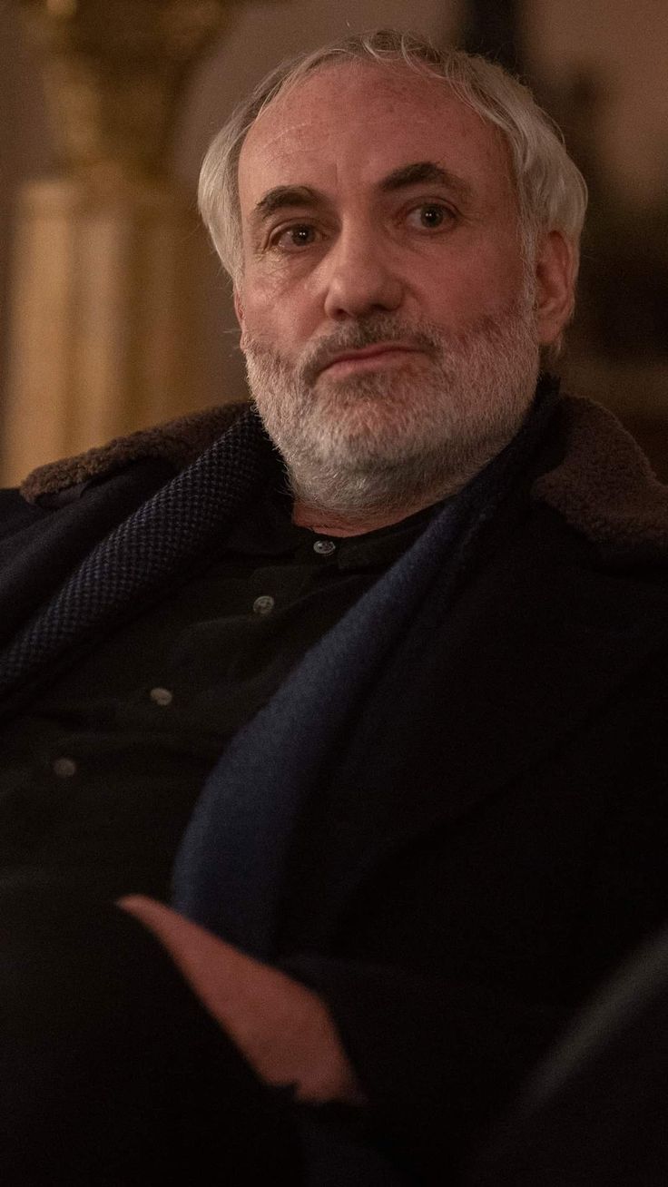 an older man with white hair and beard sitting in a chair looking at the camera