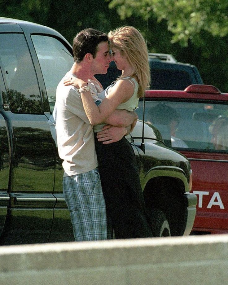 a man and woman embracing in front of cars