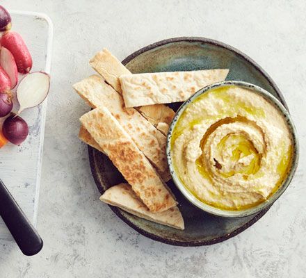 a bowl of hummus, crackers and radishes on a white table